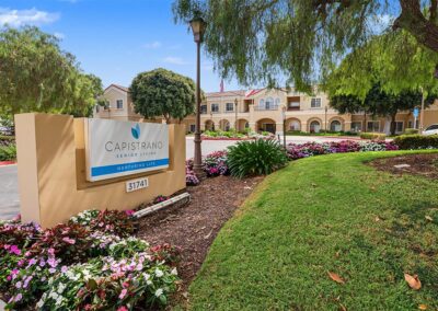 Capistrano Senior Living monument sign with colorful impatiens beds and the two-story Mediterranean-style building behind it
