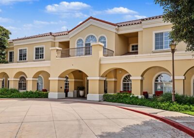 Covered arched walkway and arched balcony windows on the cream stucco exterior of the senior living community