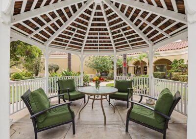 White gazebo on the courtyard patio with green-cushioned armchairs around a glass table with fresh flowers