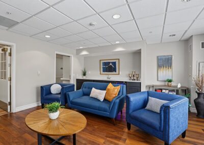 Family visiting lounge with a blue sofa and armchairs, round wood coffee table, kitchenette counter, and framed art
