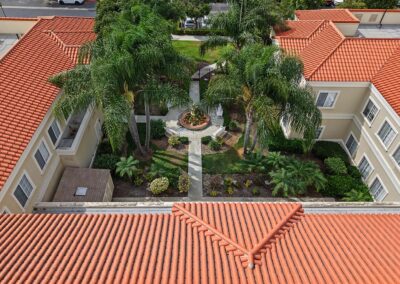 Aerial view over red tile roofs into the palm-shaded courtyard with a central fountain and garden pathways